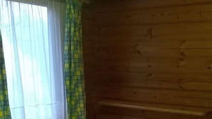 A wooden cabin bedroom with a bed, curtains, and a window. - Broxbourne Riverside Chalets (Broxbourne)