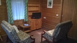 A cabin interior with two upholstered chairs, a wooden cabinet with a television, and a small table. - Broxbourne Riverside Chalets (Broxbourne)