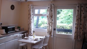 A small kitchen with a dining table, chairs, a microwave, and a window with curtains. - Broxbourne Riverside Chalets (Broxbourne)