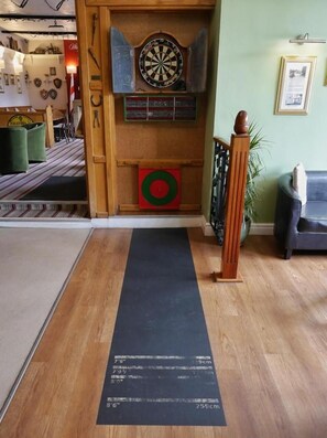 Un jeu de fléchettes, une cible et un support pour jeu de fléchettes se trouvent dans une pièce dont le sol est en bois et qui est recouverte d’un tapis noir.