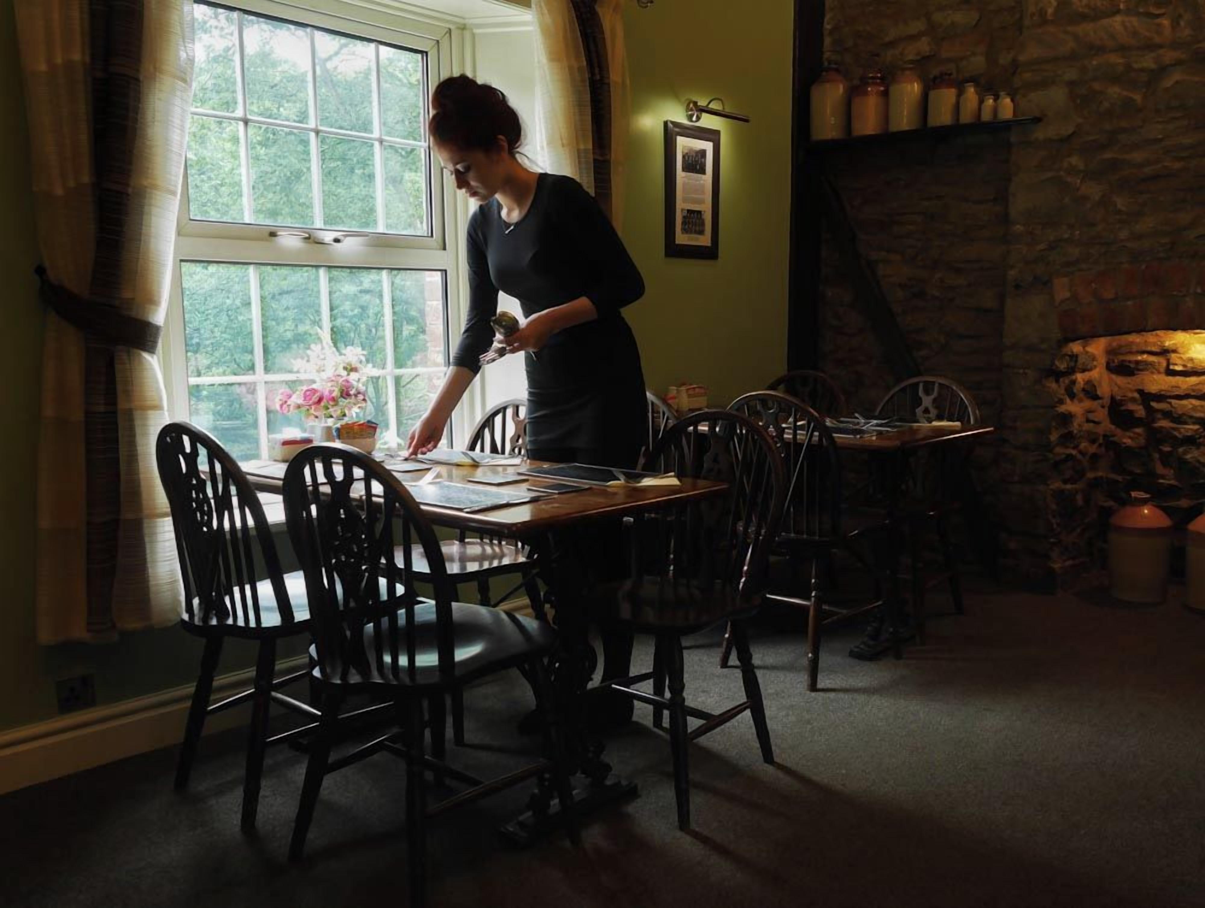 Un comedor con una mesa y sillas, una ventana con cortinas y una pared de piedra con estantes.