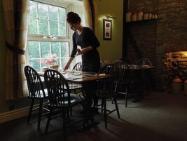 Un comedor con una mesa y sillas, una ventana con cortinas y una pared de piedra con estantes.
