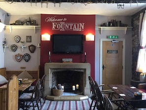 A cozy inn lobby with a fireplace, a television mounted above it, and a sign welcoming guests to the Fountain Inn Parkend. - The Fountain Inn (Lydney)