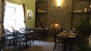 A cozy dining area with stone walls, wooden furniture, and a stone fireplace. - The Fountain Inn (Lydney)