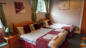 A hotel room with two beds, a nightstand, a chair, and a window with curtains. - The Fountain Inn (Lydney)