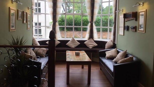A cozy room with a large window, a sofa, a table, and framed pictures on the walls. - The Fountain Inn (Lydney)