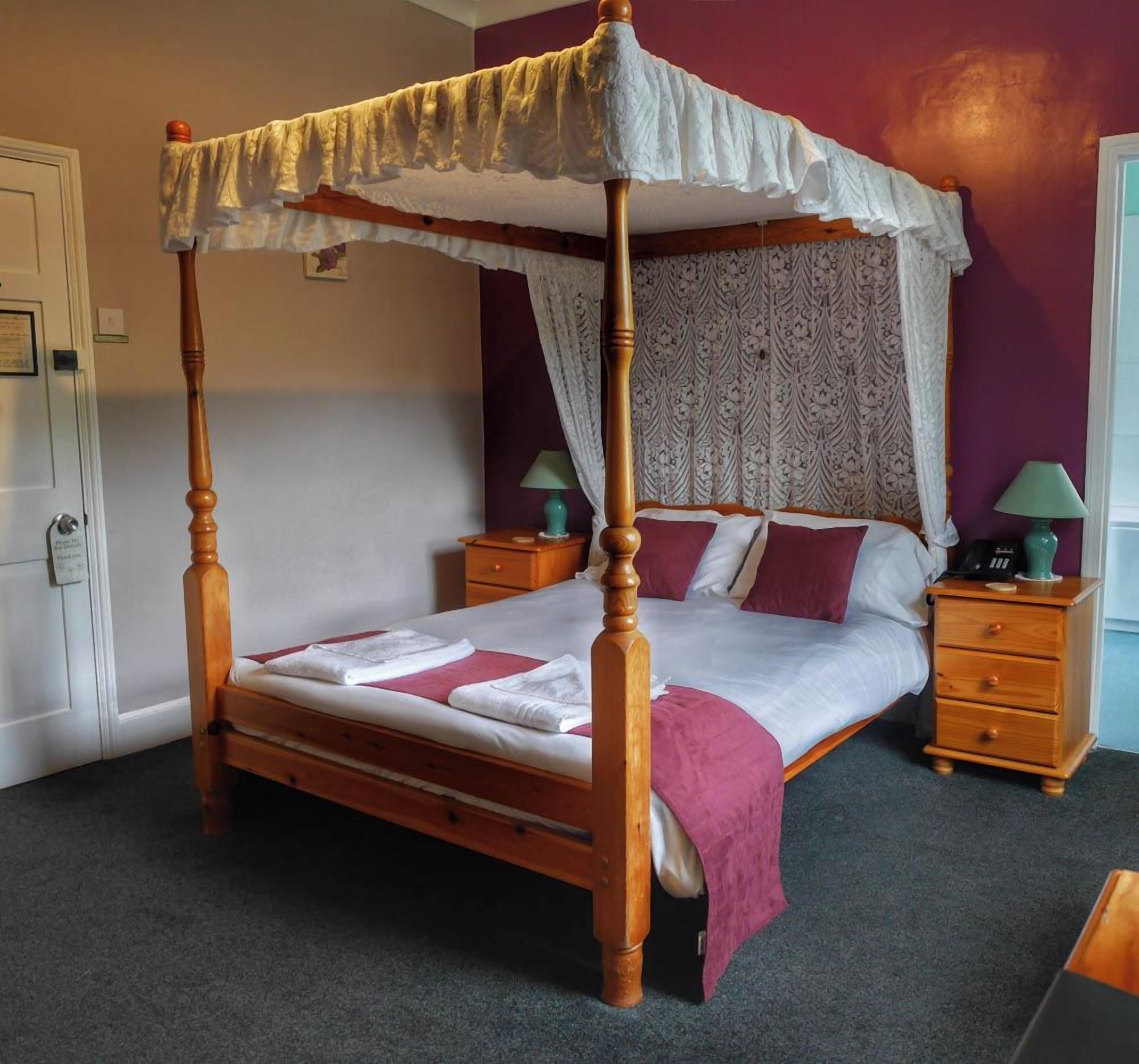 A four-poster bed with a canopy, a bedside table with a lamp, and a nightstand with a lamp.