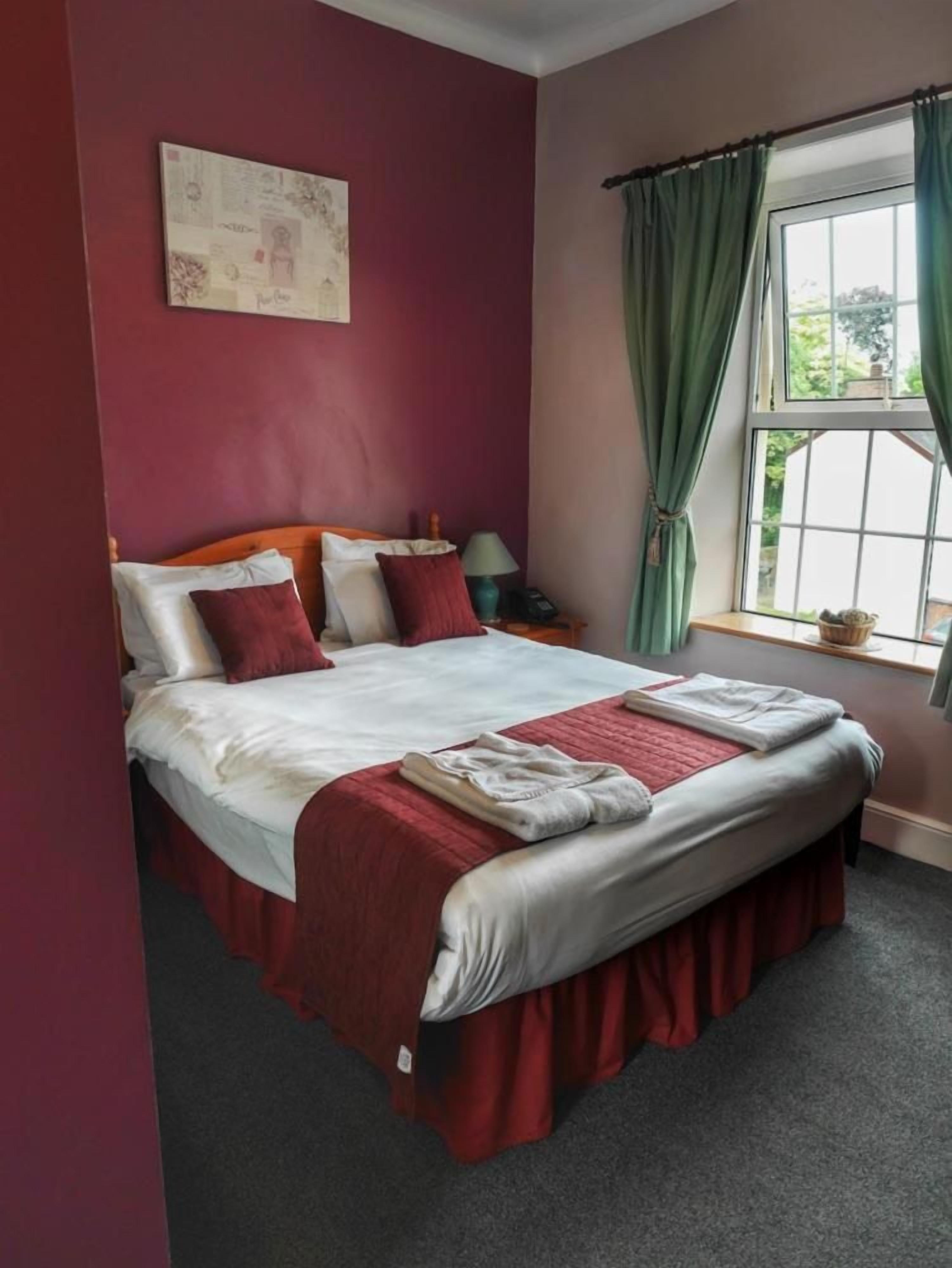 A neatly made bed with a red and white bedspread, a wooden headboard, and a window with green curtains.