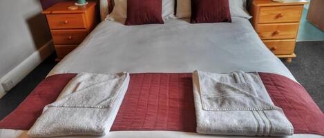 Una cama bien hecha con un cabecero estampado, dos mesitas de noche con lámparas y una alfombra a rayas rojas y blancas.