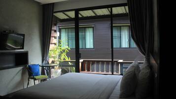 Una habitación de hotel con cama, una silla, una mesita, televisión y balcón con barandilla.