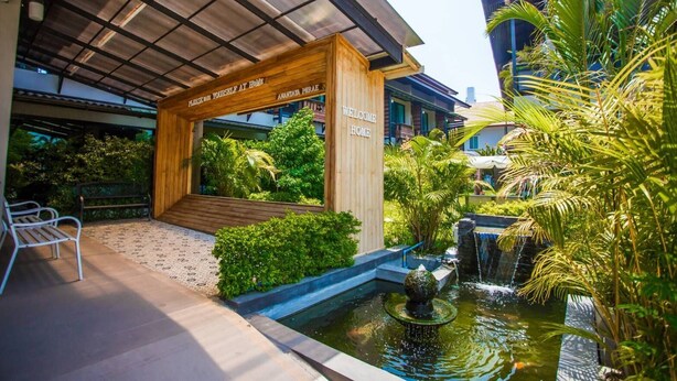 A modern hotel entrance with a wooden archway, a small garden area, and a water feature. - Anantaya Home Phare (Sung Men)