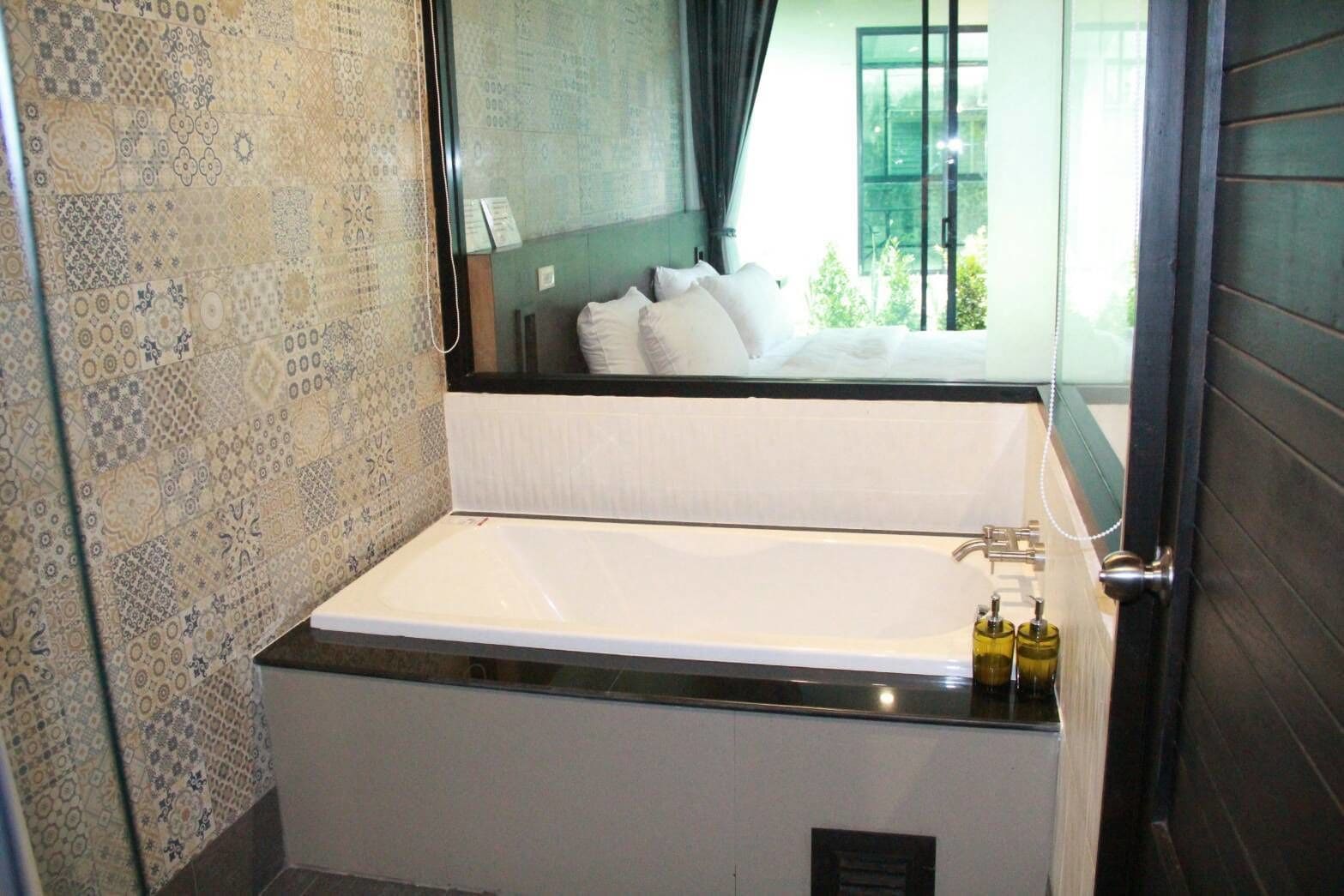 A modern bathroom with a large bathtub, a shower area, and a window with a view of a balcony.