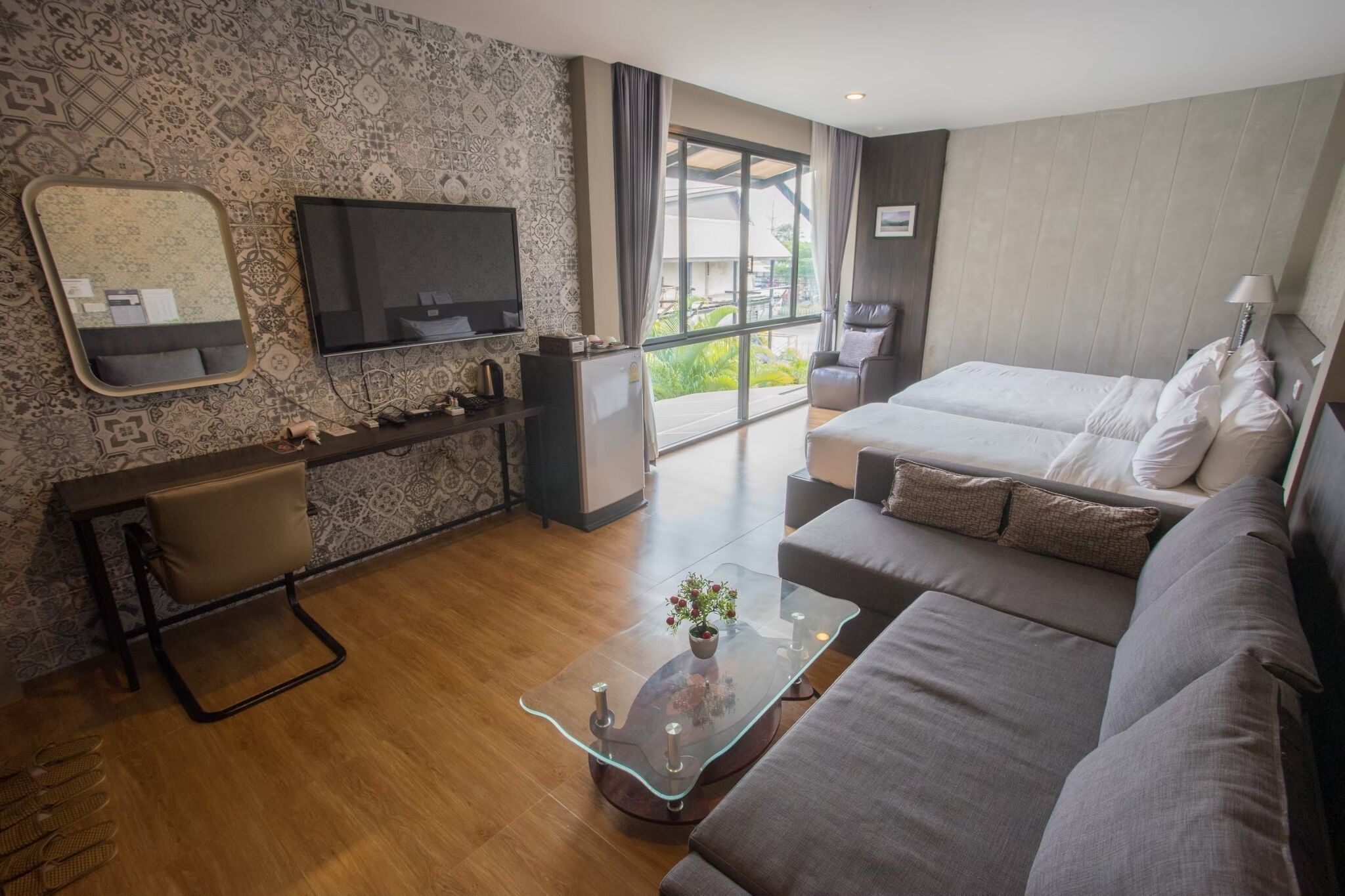 A modern hotel room with a sofa, a TV, a desk, and a large window.