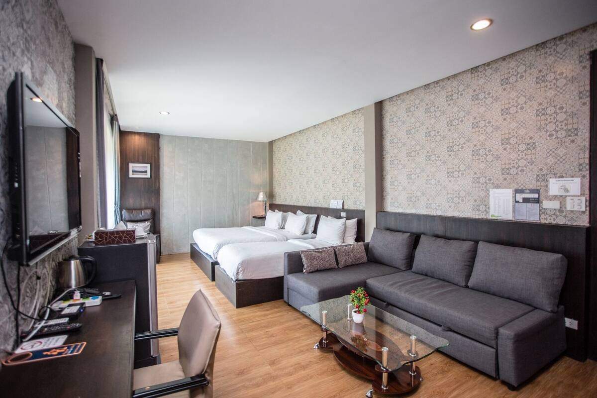 A modern hotel room with two beds, a sofa, a desk, and a TV.