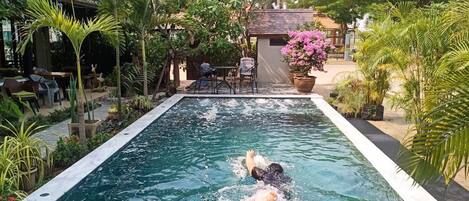 A swimming pool surrounded by lush greenery and a small building with outdoor seating.