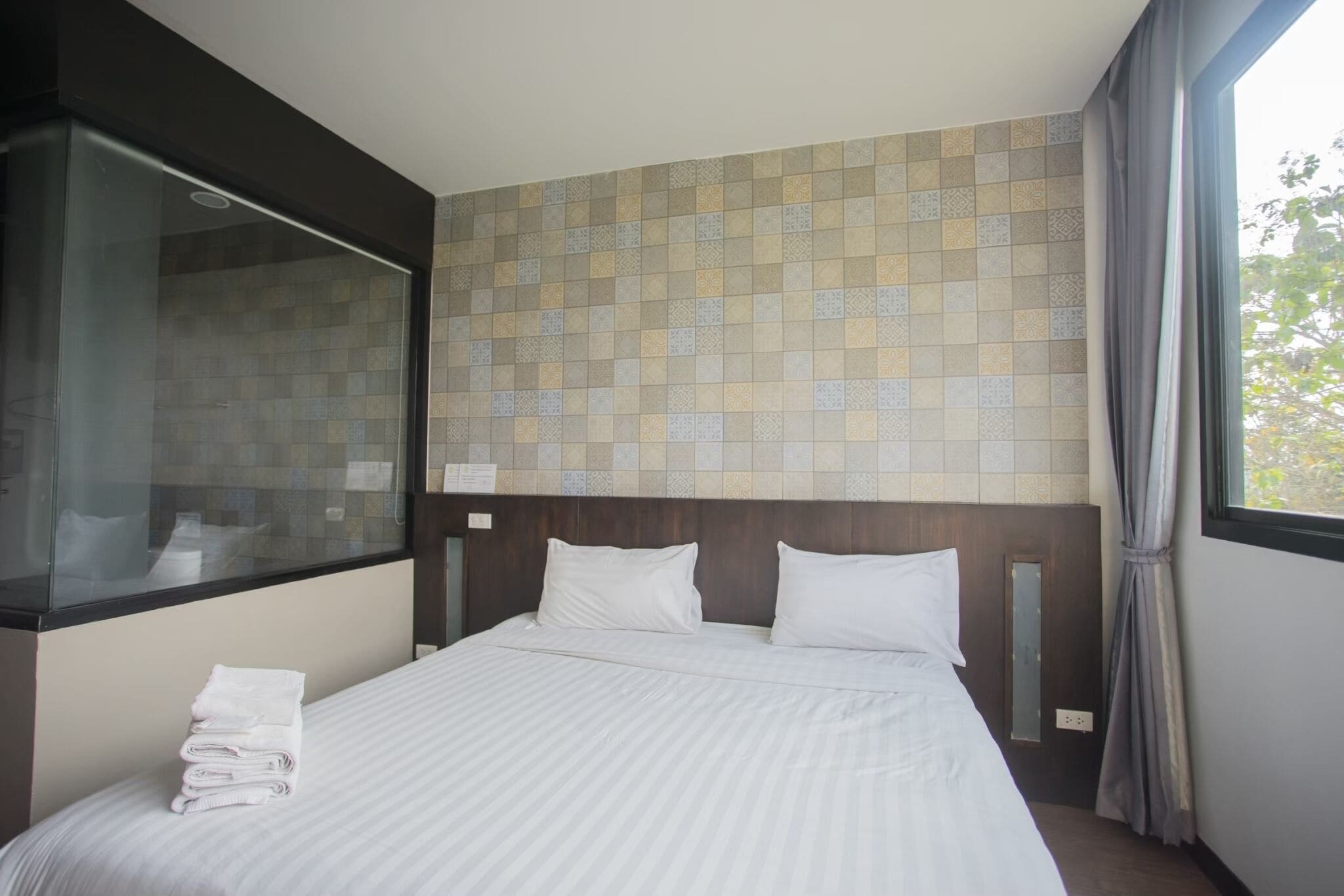 Una habitación de hotel con cama, ventana, ducha y pared con azulejos.