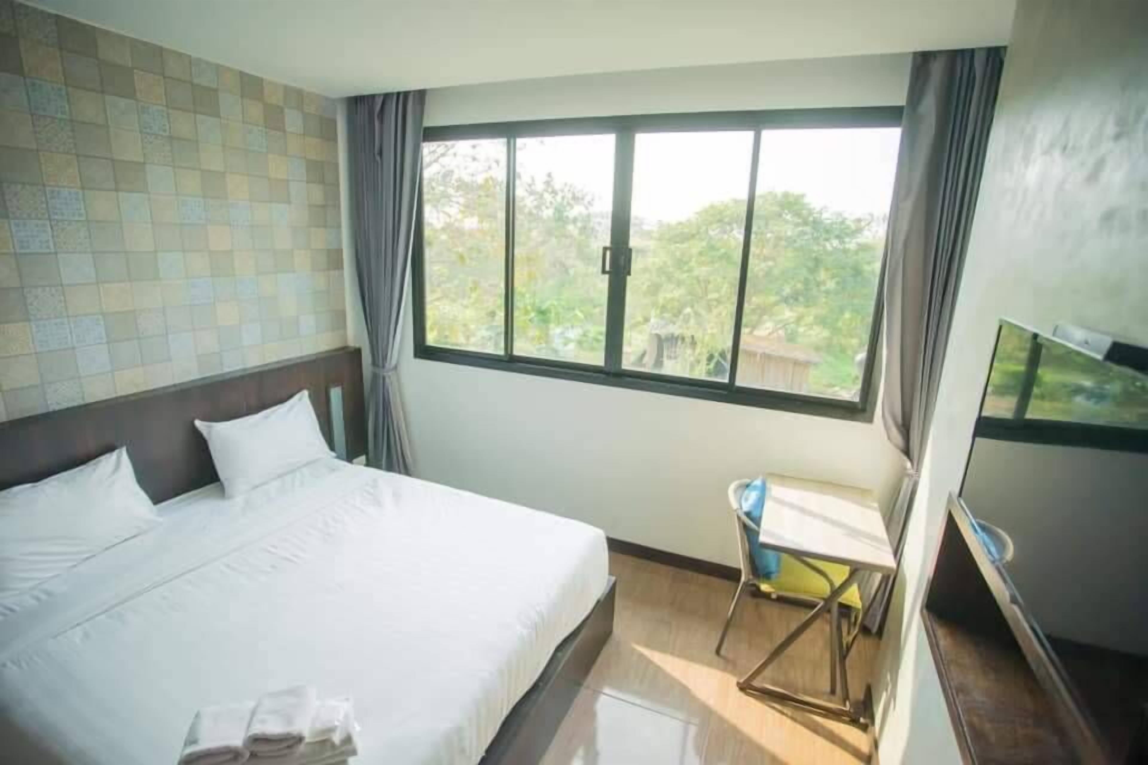 Habitación de hotel con una cama grande, un escritorio pequeño, un televisor y una ventana con vista a zonas verdes.