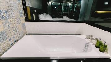 Un bany modern amb una banyera gran, un mirall i un lavabo amb dosificadors de sabó verd.