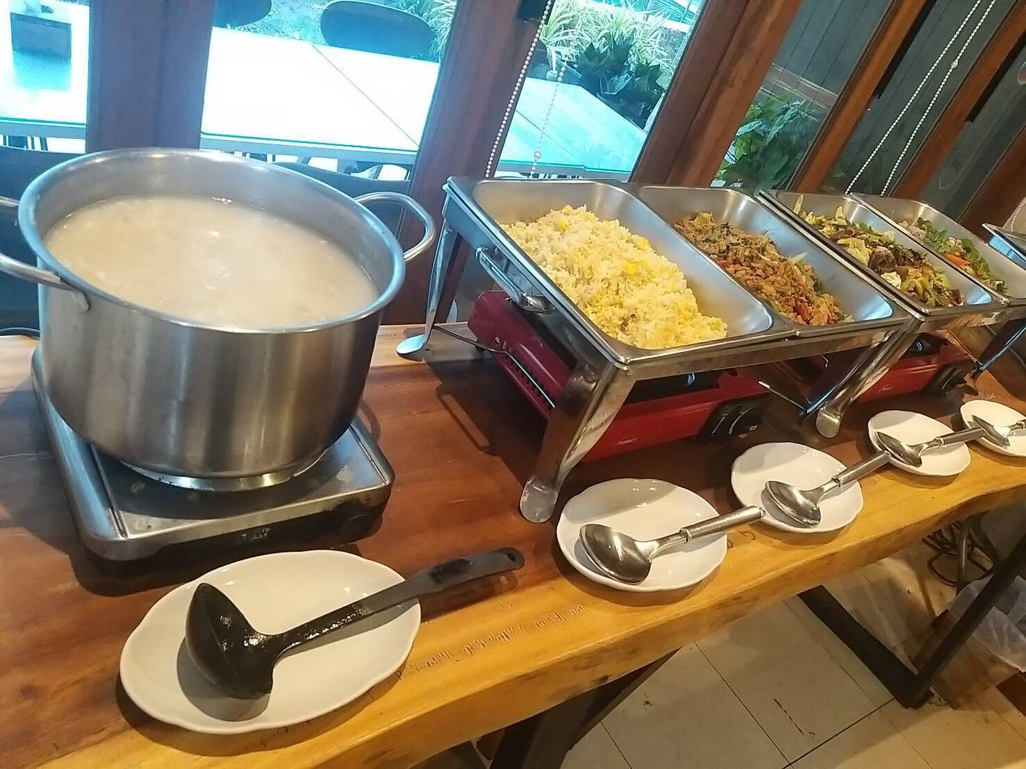 A buffet setup with a large pot of soup, rice, and various dishes in metal containers.
