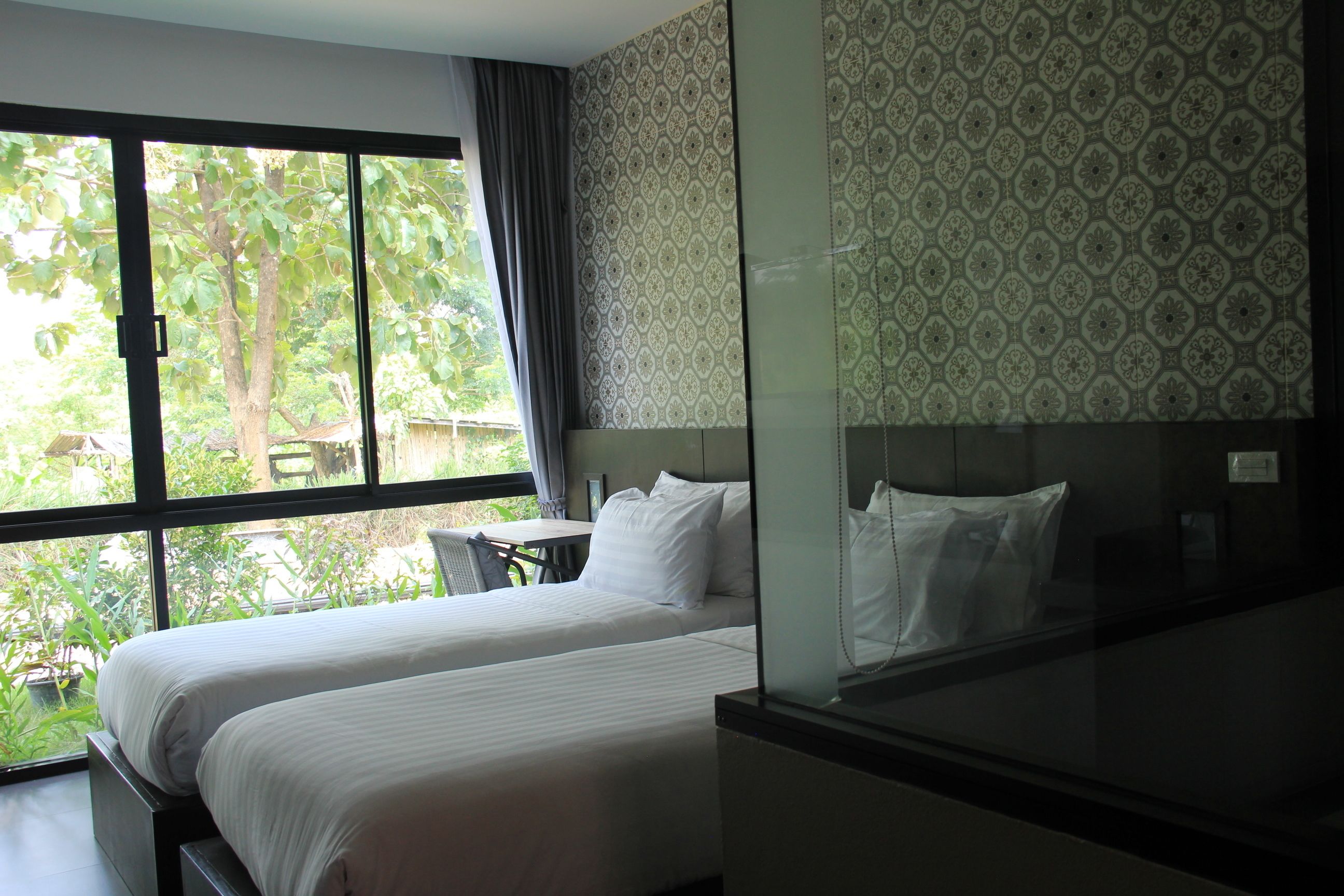 Een hotelkamer met twee bedden, een groot raam en een kamer met een patroon op de muur.