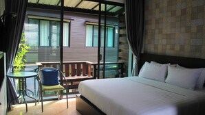 A hotel room with a large bed, a small table with a chair, and a balcony with a view of a building. - Anantaya Home Phare (Sung Men)