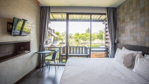 A hotel room with a bed, a small table with a chair, a TV mounted on the wall, and a balcony with a view of the outside. - Anantaya Home Phare (Sung Men)