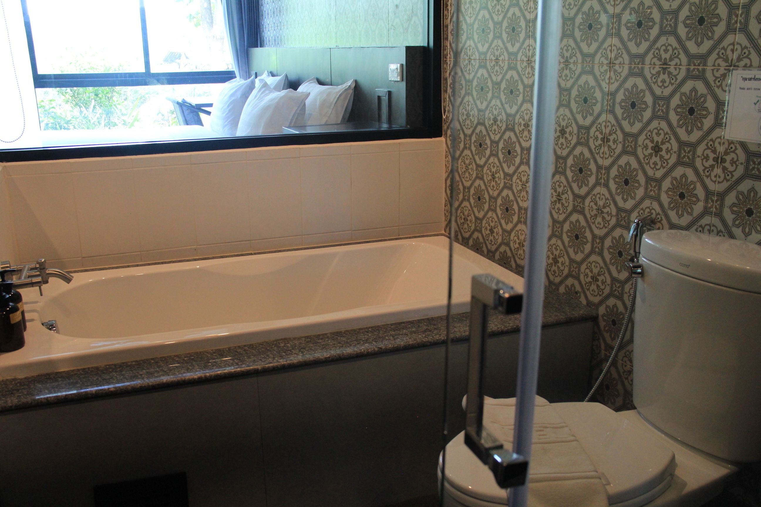 A bathroom with a bathtub, toilet, and a window with a view of greenery outside.