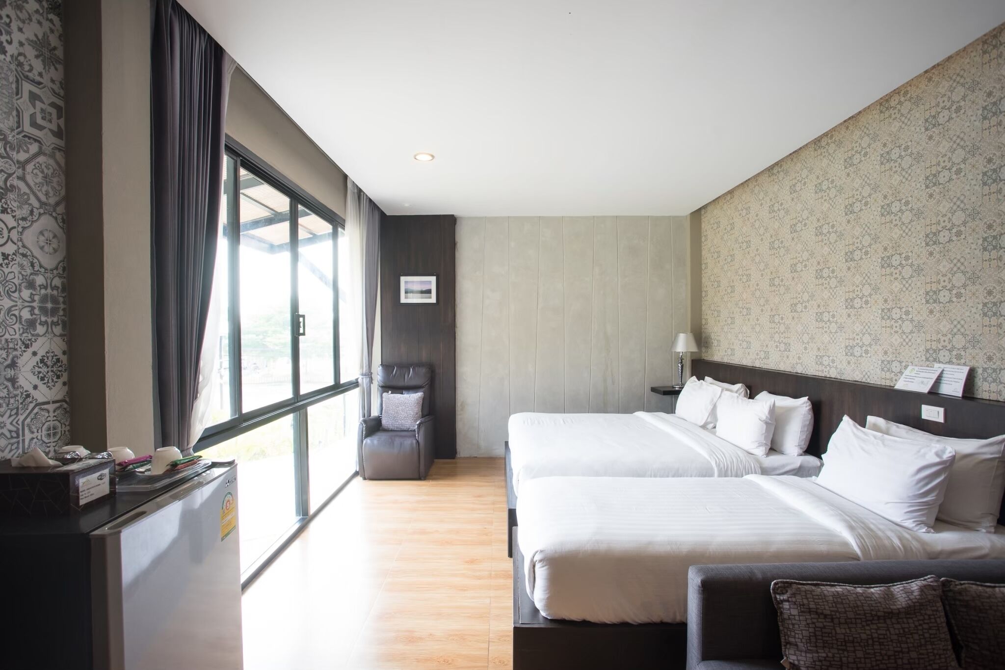 Una habitación de hotel con dos camas, un escritorio, una silla y un ventanal grande.
