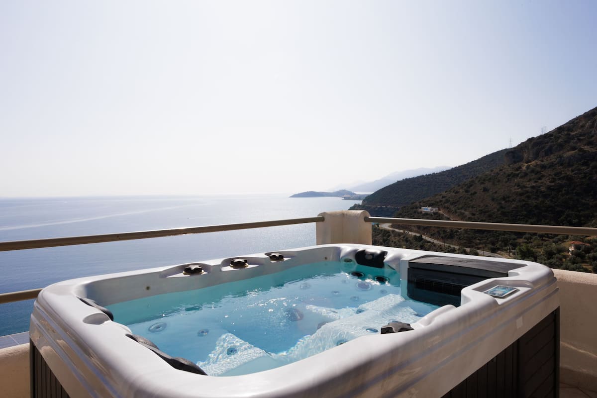 A hot tub on a balcony with a view of the sea and a mountainous landscape.