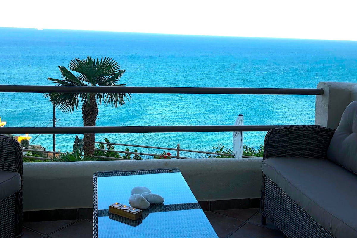A balcony with a view of the sea, a table with stones and candles, and wicker furniture.