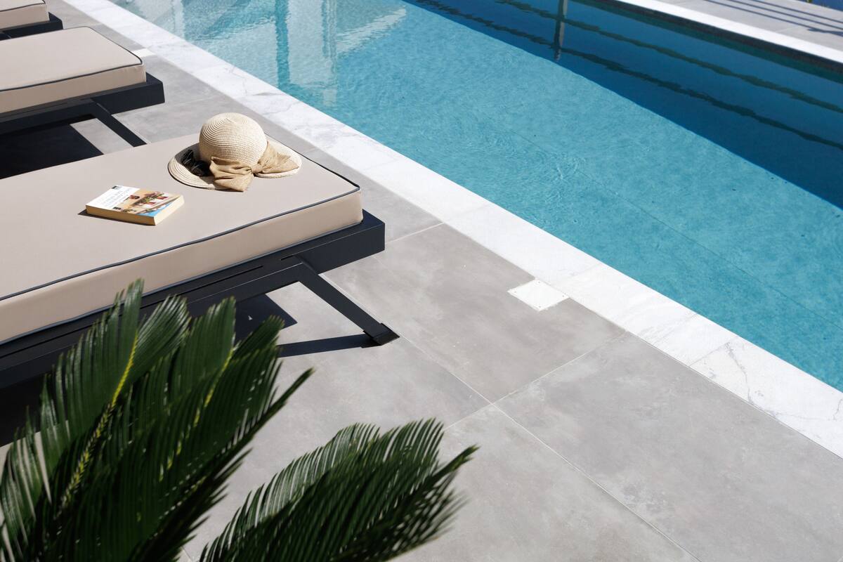 A poolside area with lounge chairs, a hat, and a book.