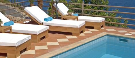 Una piscina al aire libre, sombrillas, sillones reclinables de piscina