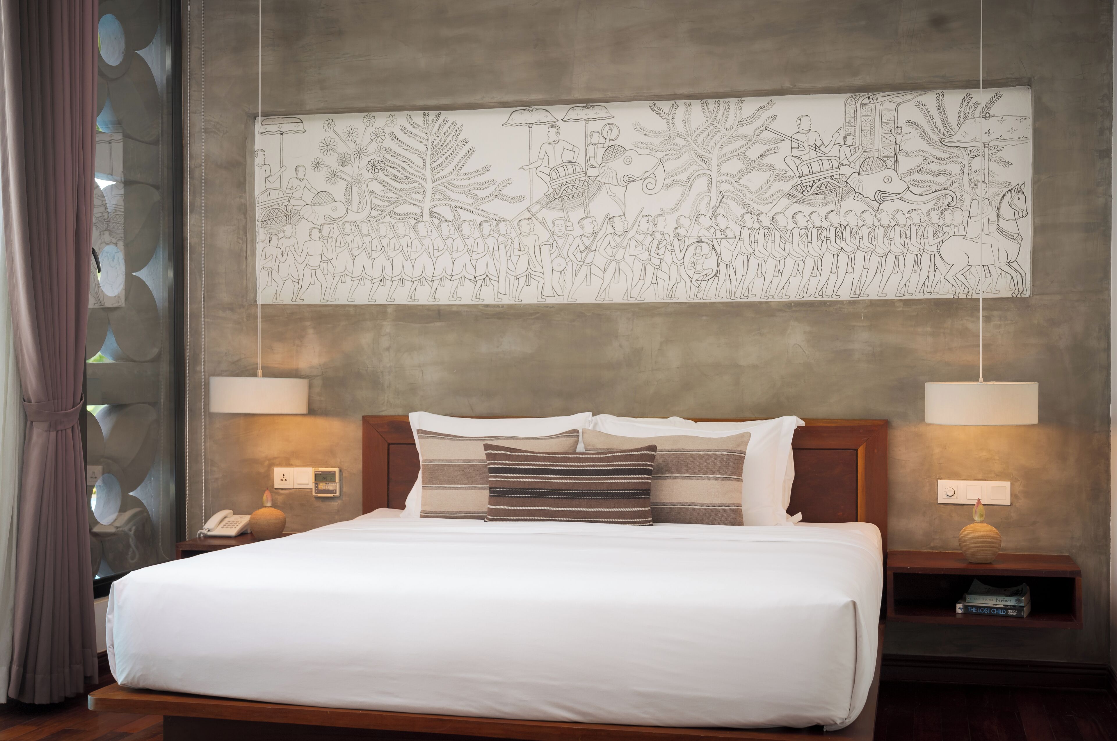 A hotel room with a large bed, two bedside tables with lamps, a wall-mounted artwork depicting a procession, and a window with a curtain.