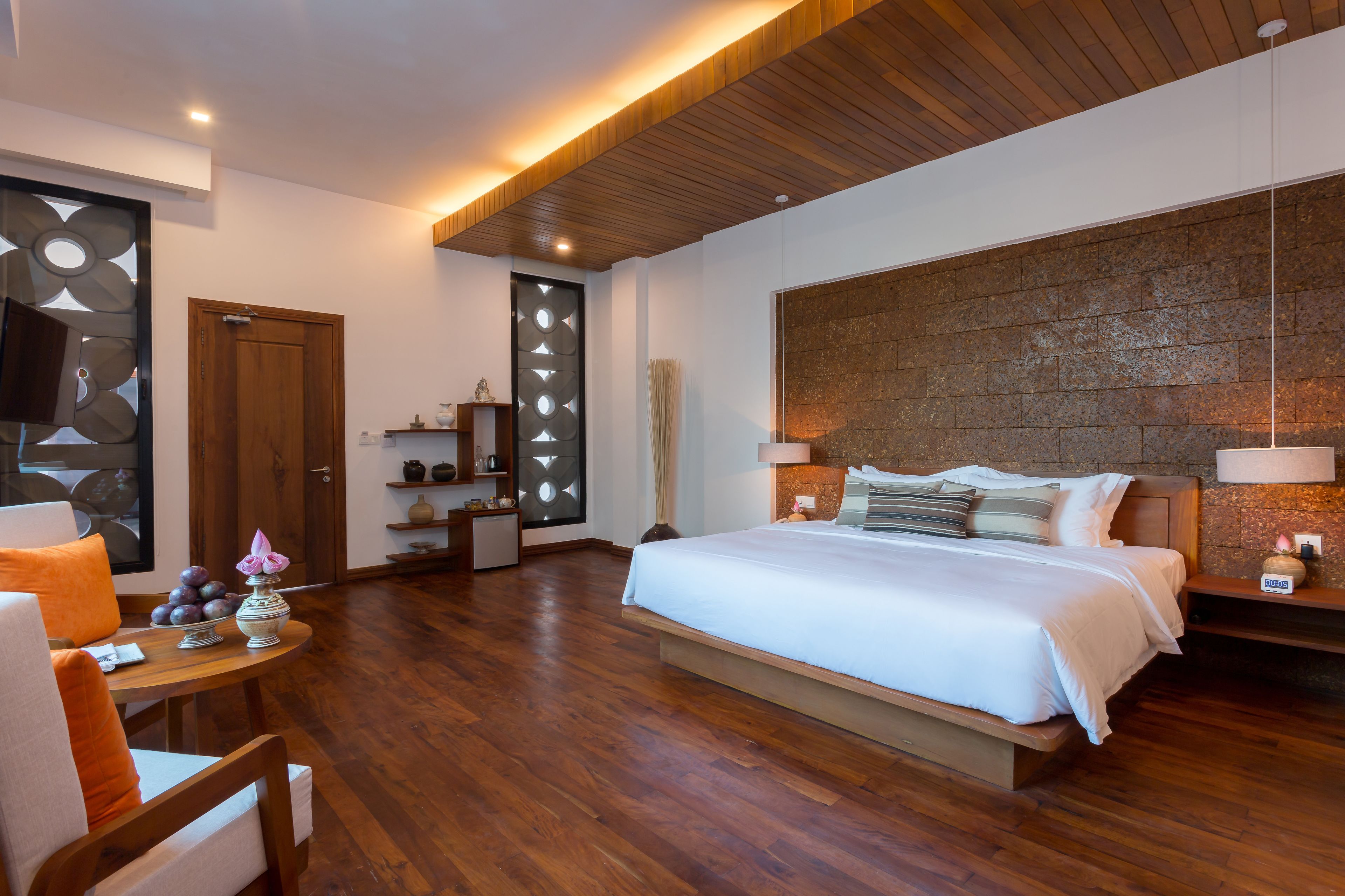 A modern bedroom with a large bed, wooden flooring, a built-in headboard, and a stone accent wall.