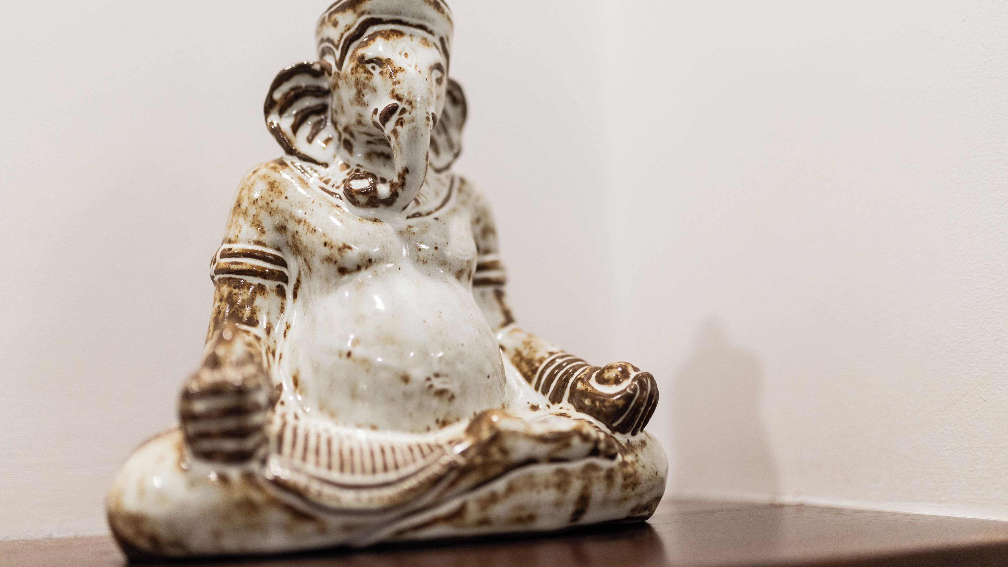 Una estatua de cerámica blanca con detalles marrones, sobre una superficie de madera frente a una pared lisa.