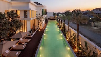 A swimming pool with lounge chairs, a modern building, and a view of the sunset.