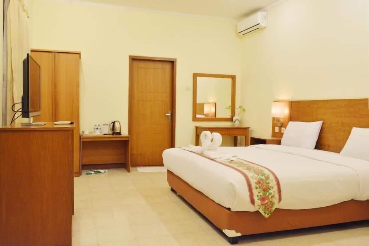A hotel room with a bed, a desk, a television, a mirror, and an air conditioning unit.