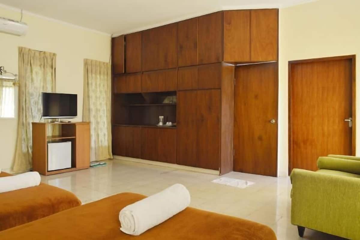 A hotel room with two beds, a TV, a wardrobe, and a green armchair.