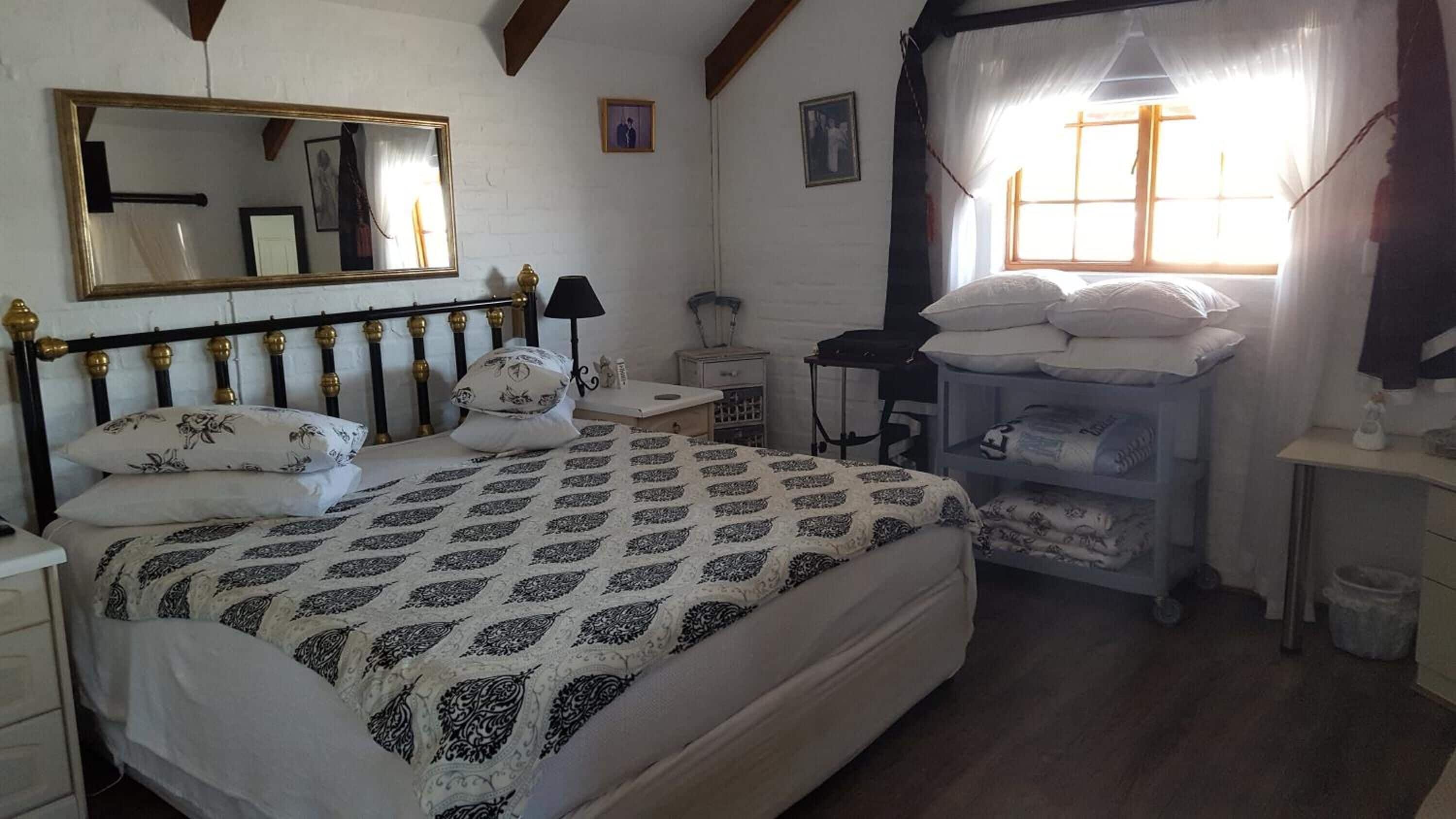 Een slaapkamer met een bed, nachtkastje, kapstok en een spiegel, met gordijnen voor het raam.