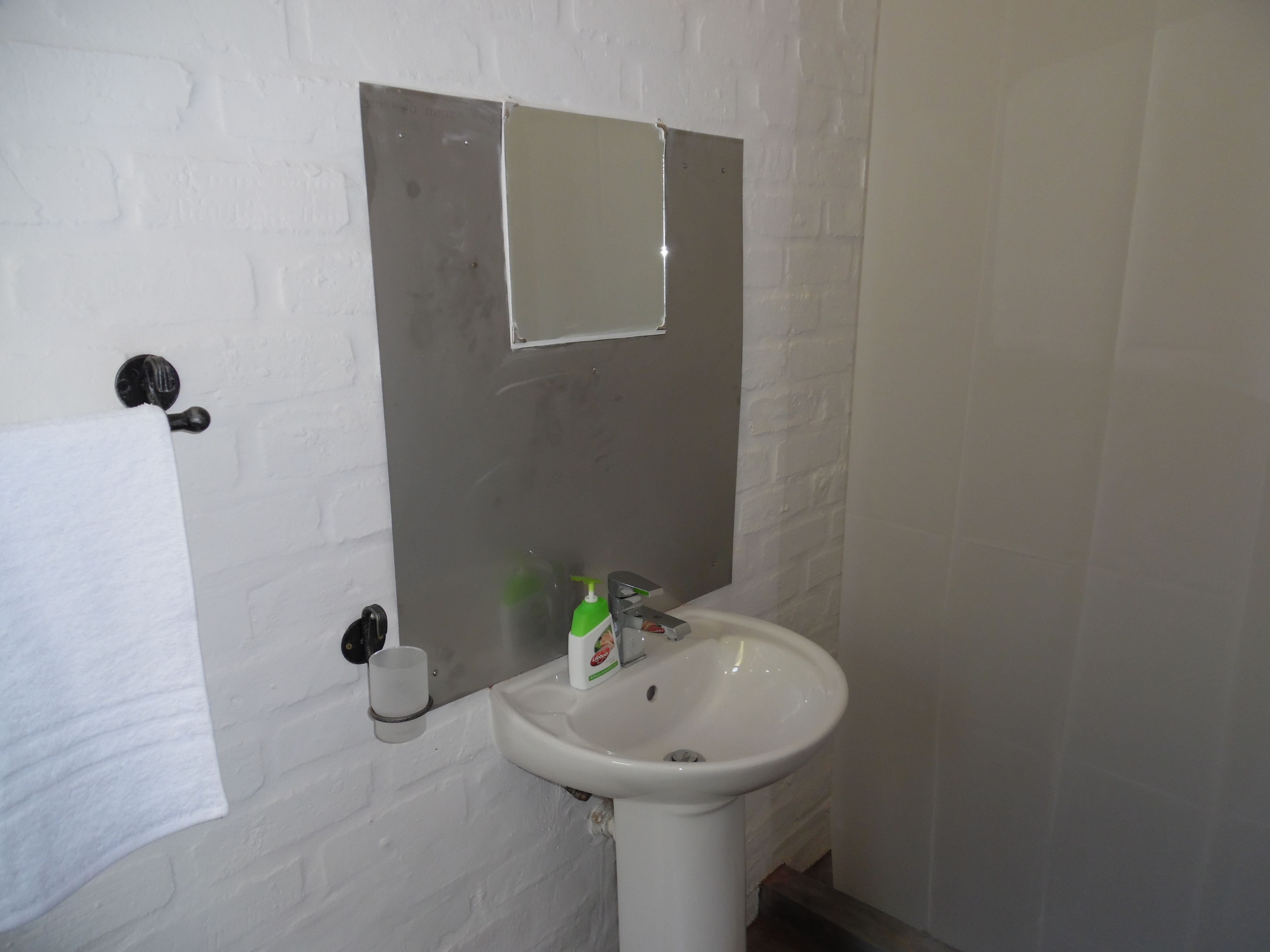 Un baño con lavamanos blanco, un espejo y una toalla colgada en un perchero.