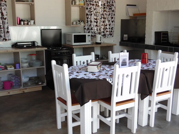 Una cocina compacta con armarios blancos, un microondas, un tostador y una estufa. Hay sillas blancas alrededor de una mesa con un mantel individual.