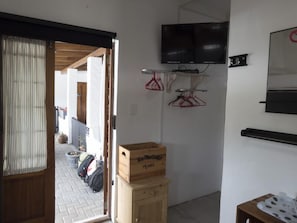 Ein Zimmer mit einem Holzkasten, einem an der Wand montierten Fernseher und einer Tür zu einem Außenbereich mit gefliestem Boden und einem hängenden Kleiderhaken.