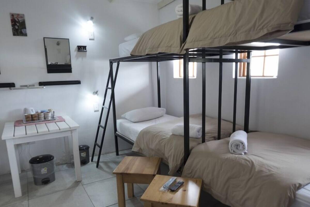 Ein Schlafsaalzimmer mit Etagenbetten, einem kleinen Tisch mit einer Fernbedienung, einem Mülleimer und einem Spiegel an der Wand.