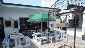 An outdoor patio area with white tables and benches, a green umbrella, and a fire pit. - Myrtles Retreat (Still Bay)