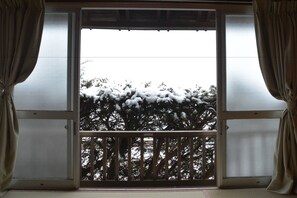 Una habitación con una puerta corrediza de vidrio que da a un balcón. El balcón tiene barandilla de madera y está rodeado de paneles de vidrio esmerilado.