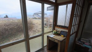 A room with large sliding glass doors, a wooden desk with a plant, and a view of a rural landscape.