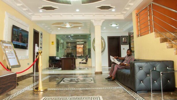 A hotel lobby with a reception desk, a waiting area with a black leather couch, and a staircase. - Kapino Suites (Abuja)
