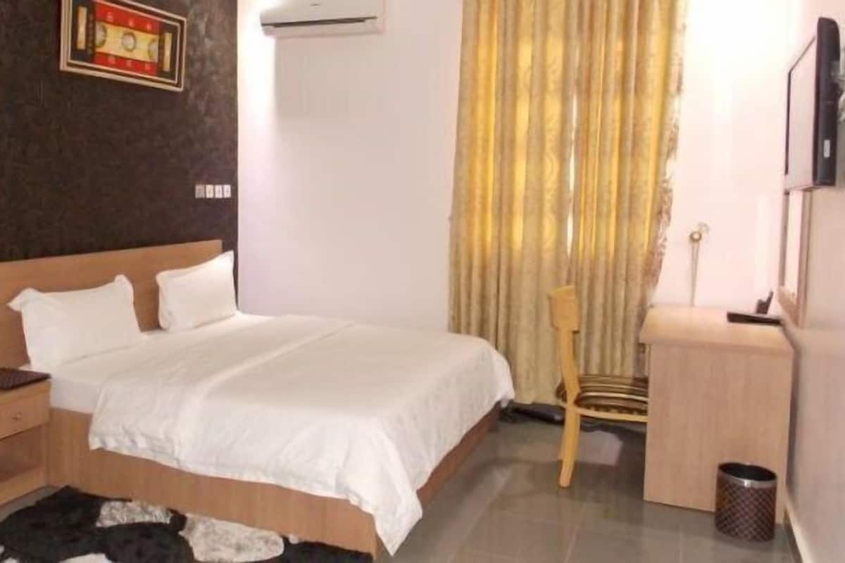 A neatly arranged hotel room with a large bed, bedside table, and a chair.