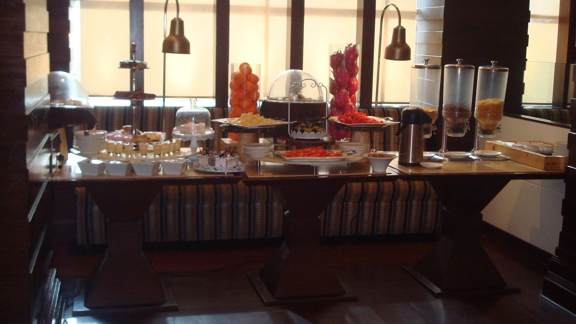 A buffet setup with various food items and beverages, including a cake on a stand, bowls of fruit, and a coffee station.