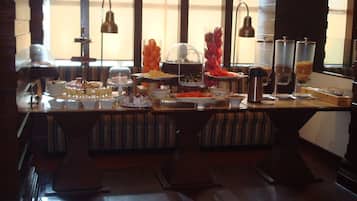 A buffet setup with various food items and beverages, including a cake on a stand, bowls of fruit, and a coffee station.